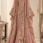 Blush pink embroidered ethnic dress with intricate floral embellishments, sheer sleeves, and an embellished flowing dupatta displayed on a hanger