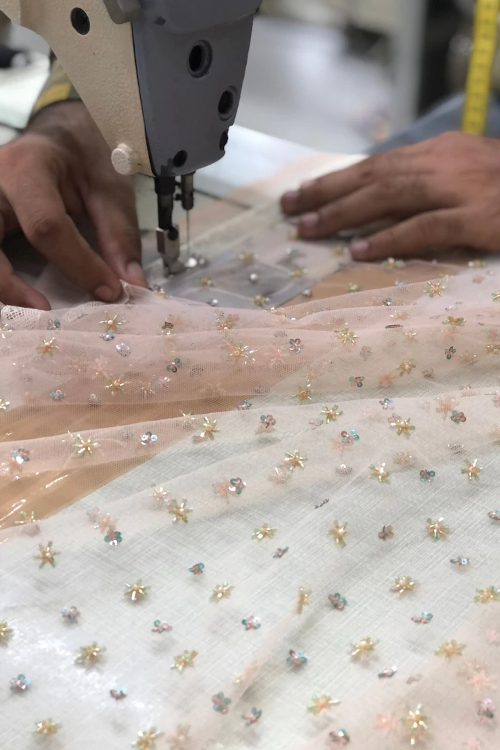 Close-up of a tailor sewing delicate embellished net fabric with floral sequin detailing using an industrial sewing machine