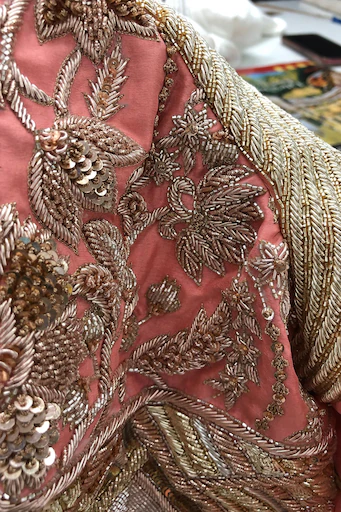 Close-up of intricate gold and rose-gold floral beadwork and sequin embroidery on pink fabric