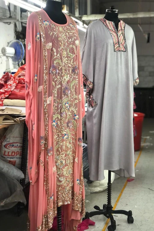 Pink embroidered ethnic dress and grey kurta displayed on mannequins in a garment workshop